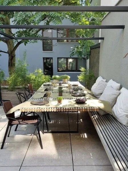 Terraza moderna al aire libre con arbol y mesa de comedor con banco largo