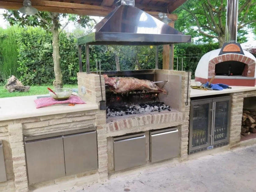 Asador de ladrillos estilo mediterráneo con un toque moderno con nevera y asador giratorio