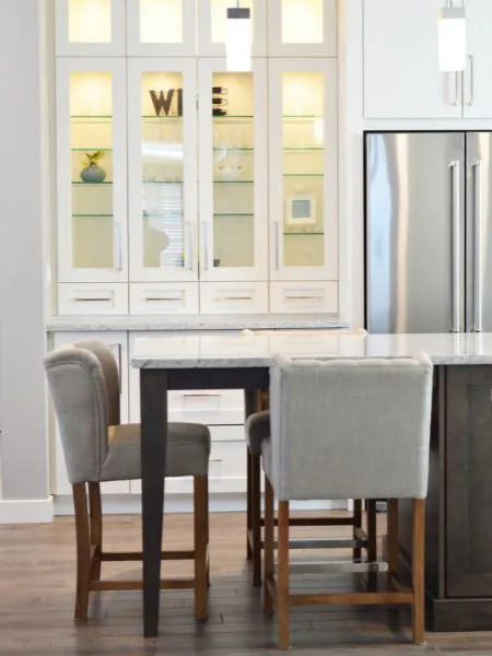 cocina blanca con vitrina isla y taburetes tapizados y patas de madera